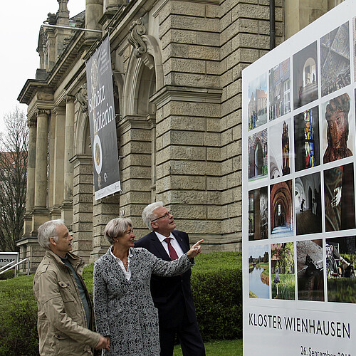 Drei Personen stehen vor einer großen Foto-Installation, im Hintergrund ist die Fassade des Landesmuseums Hannover zu sehen.