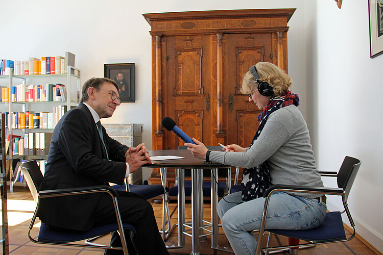 Frau mit Mikrofon und Kopfhörern interviewt Mann in einem Büroraum