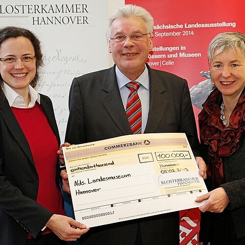 Zwei Frauen und ein Mann, Klosterkammer-Präsident Hans-Christian Biallas, halten gemeinsam einen übergroßen symbolischen Scheck in den Händen.
