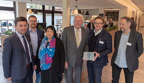 Sechs Personen, darunter Klosterkammer-Präsident Hans-Christian Biallas, stehen vor einem modernden Café in der KRH Psychiatrie Langenhagen.