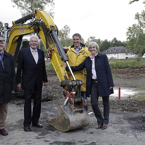 Eine Gruppe von Personen, darunter ein Frau, stehen vor einem Bagger.