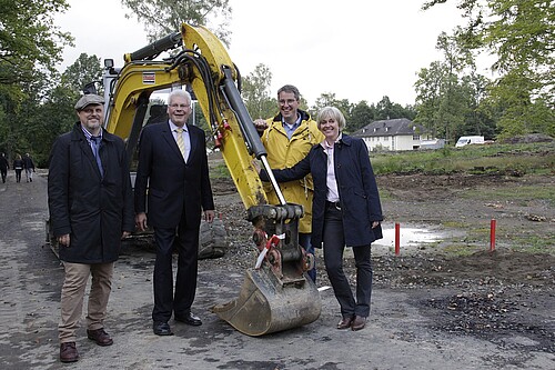 Eine Gruppe von Personen, darunter ein Frau, stehen vor einem Bagger.