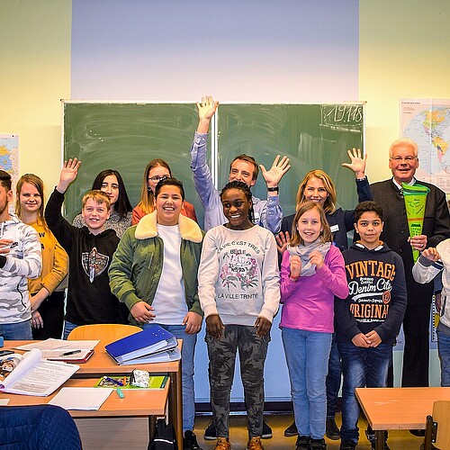 Eine Gruppe von Realschülerinnen und -schülern und Erwachsene stehen in einem Klassenraum.