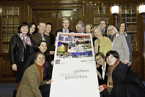 Eine Gruppe von Personen hält ein Werbebanner in den Händen mit der Überschrift: Wegweiser zu Stiftungen in Hannover.