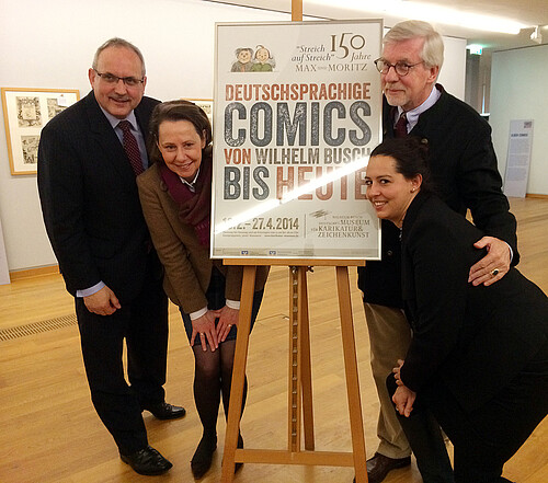 Zwei Männer und zwei Frauen, darunter Anna Mohr, Dezernentin in der Abteilung Förderungen, stehen vor einem Plakat des Wilhelm-Busch-Museums.