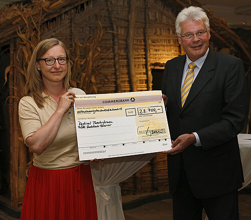 Eine Frau und ein Mann, Klosterkammer-Präsident Hans-Christian Biallas, halten einen symbolischen Scheck in den Händen.