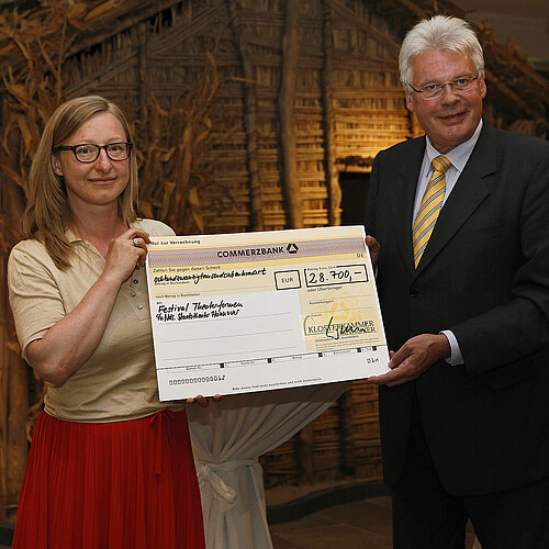 Eine Frau und ein Mann, Klosterkammer-Präsident Hans-Christian Biallas, halten einen symbolischen Scheck in den Händen.