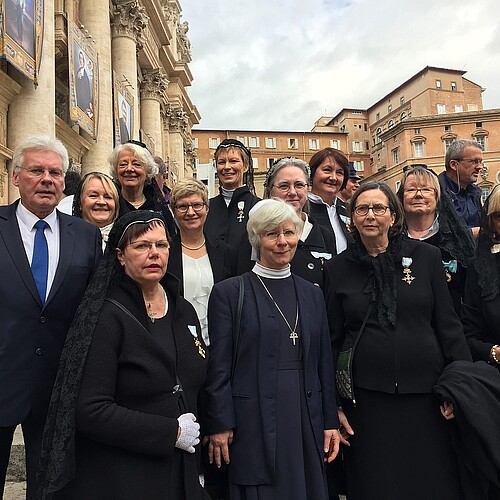 Ein Herr, Klosterkammer-Präsident Hans-Christian Biallas, und elf Damen, teilweise in traditioneller Bekleidung, stehen gemeinsam auf einem Platz. Im Hintergrund ragen Sandsteingebäude hervor.