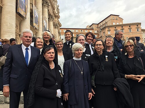 Ein Herr, Klosterkammer-Präsident Hans-Christian Biallas, und elf Damen, teilweise in traditioneller Bekleidung, stehen gemeinsam auf einem Platz. Im Hintergrund ragen Sandsteingebäude hervor.