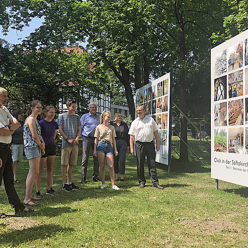 Zwei große Foto-Tafeln zu dem Foto-Projekt "Click in der Stiftskirche Wunstorf" sind nahe der Stiftskirche aufgestellt. Zur Eröffnung am 18.06.2021 kamen Schülerinnen und Schüler, die bei den Workshops dabei waren.