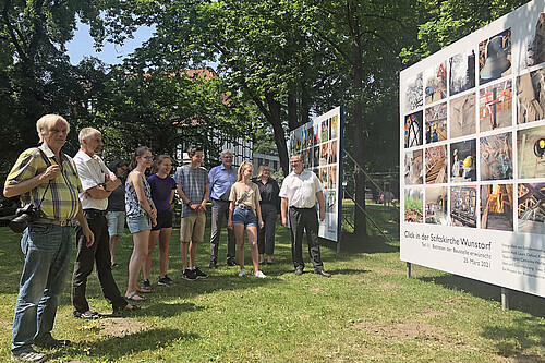 Zwei große Foto-Tafeln zu dem Foto-Projekt "Click in der Stiftskirche Wunstorf" sind nahe der Stiftskirche aufgestellt. Zur Eröffnung am 18.06.2021 kamen Schülerinnen und Schüler, die bei den Workshops dabei waren.
