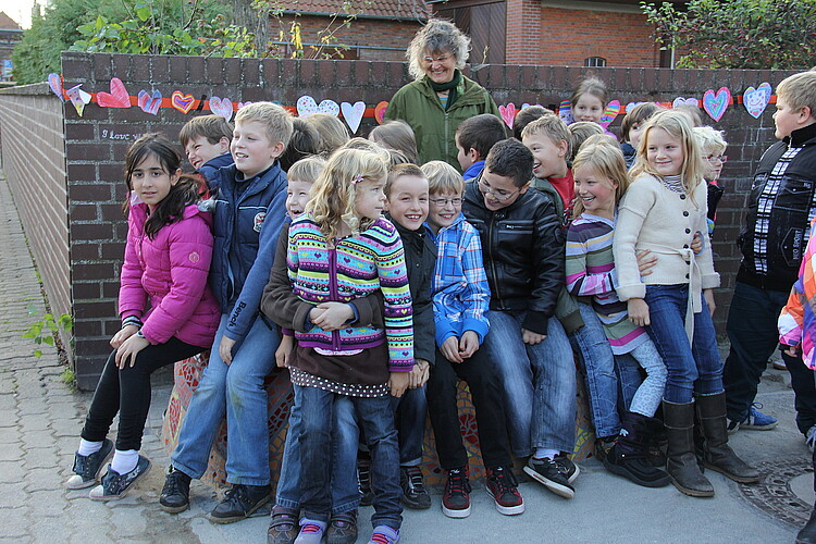 Jungen und Mädchen einer Grundschulklasse sitzen gemeinsam auf einer Sitzskulptur.