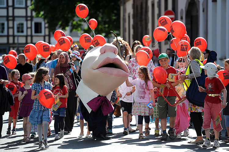 Umzug zum Familientag des Kinder- und Jugendprogramms „Händel 4 Kids!“ während der Internationalen Händel-Festspiele Göttingen: Kinder und ihre Eltern gehen zusammen mit einem verkleideten Schauspieler über eine Straße.
