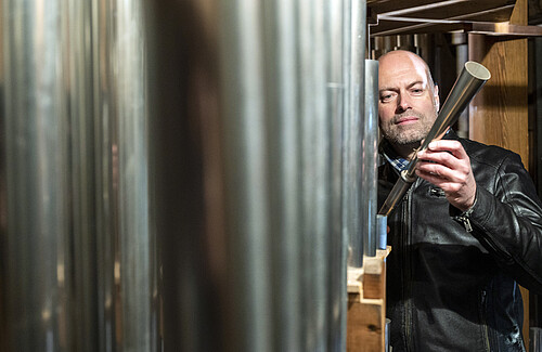Henning Voss, Kirchenmusiker an der St. Michaeliskirche, steht neben großen Orgelpfeifen.