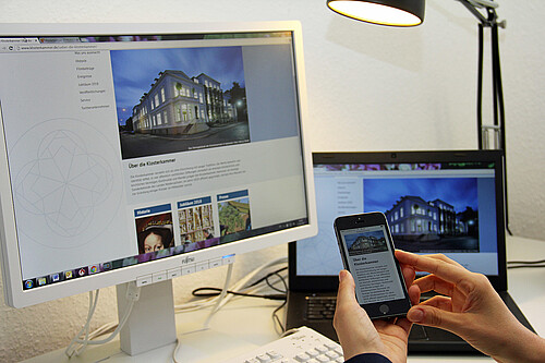 Ein Bildschirm, ein Laptop und ein Smartphone auf einem Schreibtisch - auf allen ist die neue Internetseite der Klosterkammer zu sehen.