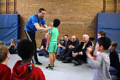 Eine Gruppe von Kindern und Erwachsenen, darunter Klosterkammer-Präsident Hans-Christian Biallas, sitzen auf dem Fußboden einer Turnhalle.