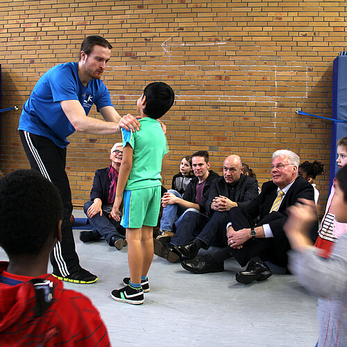 Eine Gruppe von Kindern und Erwachsenen, darunter Klosterkammer-Präsident Hans-Christian Biallas, sitzen auf dem Fußboden einer Turnhalle.