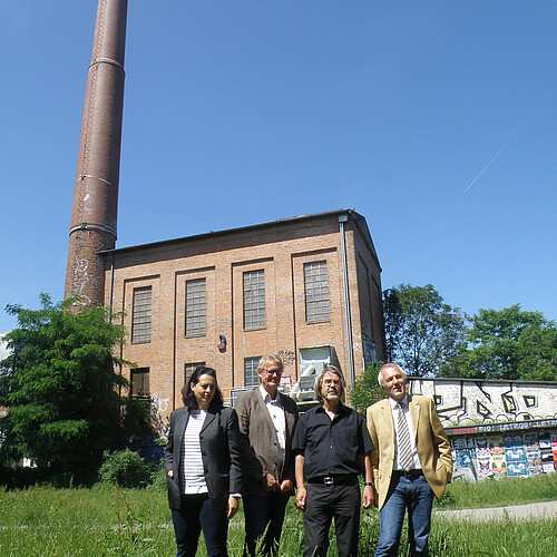 Kesselhaus mit Schornstein und quadratisches Gebäude im Hintergrund, im Vordergrund sind vier Personen, unter anderen Anna Mohr von der Klosterkammer, zu sehen.
