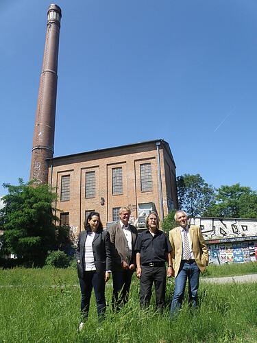Kesselhaus mit Schornstein und quadratisches Gebäude im Hintergrund, im Vordergrund sind vier Personen, unter anderen Anna Mohr von der Klosterkammer, zu sehen.