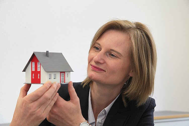 Eine Frau hält ein kleines Haus in der Hand.