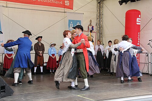 Tanzende Paare in Trachten auf einer Bühne.