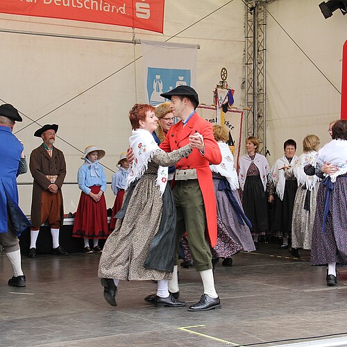 Tanzende Paare in Trachten auf einer Bühne.