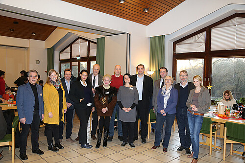 Eine Gruppe von dreizehn Männern und Frauen steht in einem geschmückten Raum.