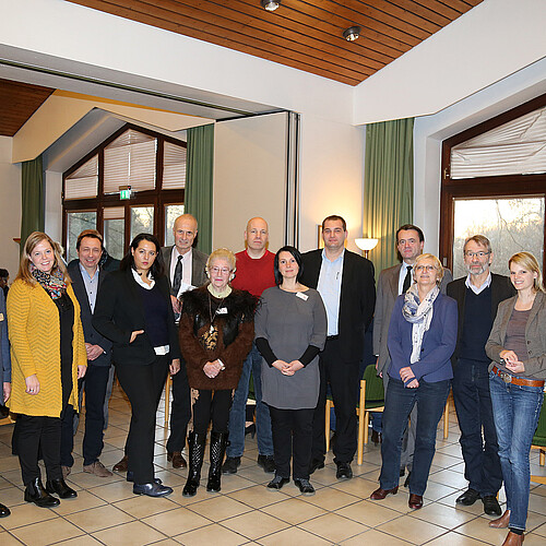 Eine Gruppe von dreizehn Männern und Frauen steht in einem geschmückten Raum.