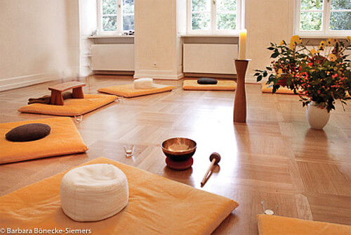 Blick in einen aufgebauten Meditationskreis im Kloster Wennigsen mit Kissen, Blumen und einer Klangschale.