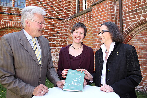 Zwei Frauen, darunter Renate von Randow, Äbtissin des Klosters Wienhausen, und ein Mann stehen gemeinsam an einem runden Tisch und präsentieren ein Buch.