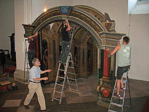 Vier Personen sind mit dem Aufbau einer mehrere Meter hohen Kulisse aus Holzteilen in einer Kirche beschäftigt.