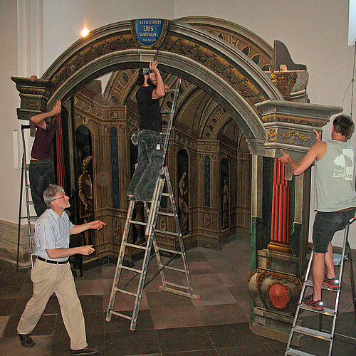 Vier Personen sind mit dem Aufbau einer mehrere Meter hohen Kulisse aus Holzteilen in einer Kirche beschäftigt.