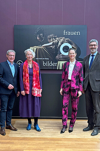 Vier Personen vor einen Ausstellungsplakat