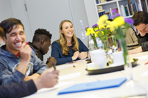Eine junge Frau sitzt an einem Tisch gemeinsam mit zugewanderten Jugendlichen.