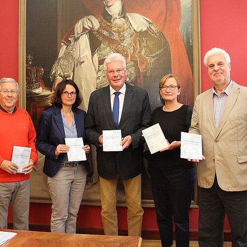 Mitarbeiter der Klosterkammer Hannover, darunter Klosterkammer-Präsident Hans-Christian Biallas, stehen zur Vorstellung der Jubiläumsschrift der Viktoria-Luise-Stiftung vor einem Ölgemälde.