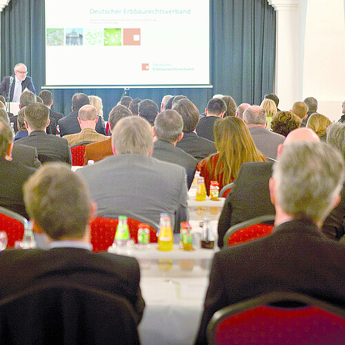 Eine Gruppe von Personen hört einem Redner am Pult zu.