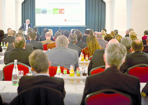 Eine Gruppe von Personen hört einem Redner am Pult zu.