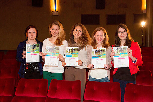 Fünf Schülerinnen, die jeweils eine Urkunde in den Händen halten, stehen zwischen Sitzreihen in einem Kino.