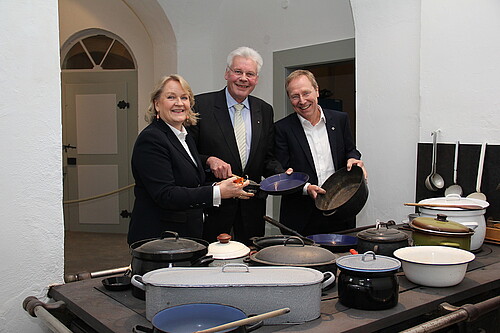 Drei Personen stehen hinter einem historischen Herd.