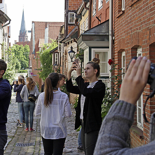 Mehrere Jugendliche stehen in einer Straße mit historischen Häusern und fotografieren.