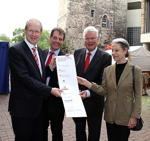 Eine Frau und drei Männer, darunter Klosterkammer-Präsident Hans-Christian Biallas, halten ein Plakat mit den Förderern der Renovierung des hannoverschen Beginenturms in den Händen.