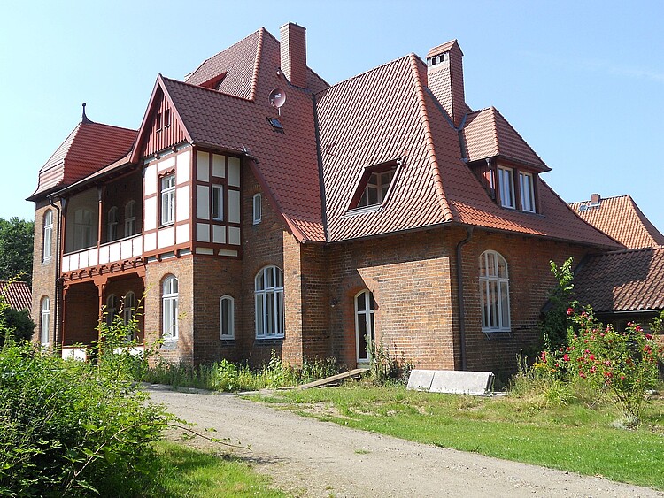 Ein großes Haus mit einer dunkelroten Dacheindeckung und verwinkelter Architektur.