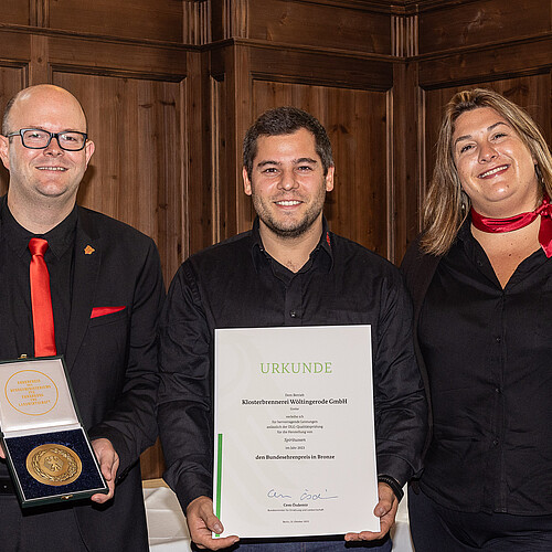 Drei Männer und zwei Frauen nebeneinander. Ein Mann hält Schachtel mit Medaille. Ein Mann hält eine Urkunde.