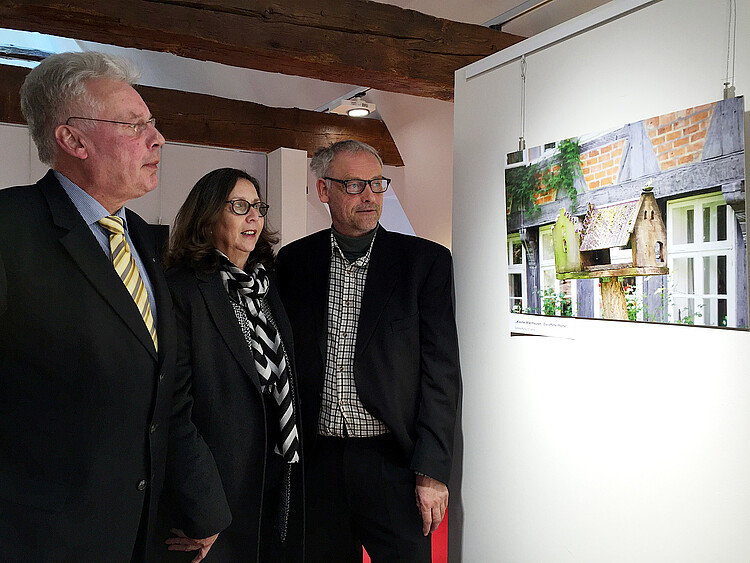 Drei Personen schauen sich ein auf eine Tafel gerucktes Foto in einem Museum an.