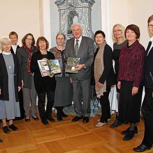 Zehn Frauen und ein Mann stehen in einem Halbkreis, zwei der Personen haben ein farbiges Magazin in der Hand.
