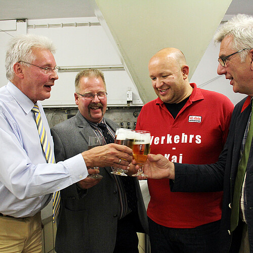 Vier Herren stoßen jeweils mit einem Glas Bier an.