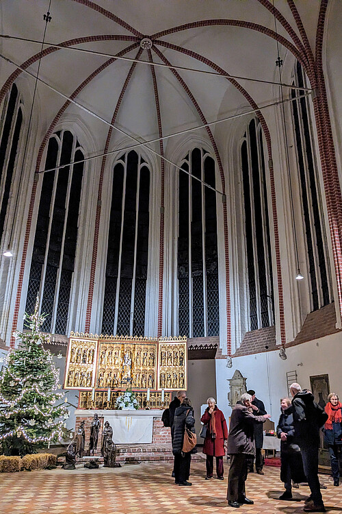 Eine Gruppe von Menschen steht in einer Kirche vor dem Altar, daneben ist ein geschmückter Weihnachtsbaum.