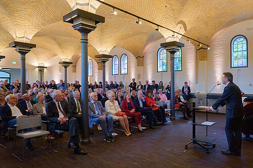 Ein Mann, Uni-Präsident Prof. Dr. Volker Epping, spricht ein Grußwort in einem Konzertsaal vor rund 150 Gästen.
