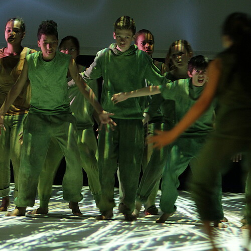 Schülerinnen und Schüler stehen gemeinsam in grünen Kostümen auf einer Bühne.