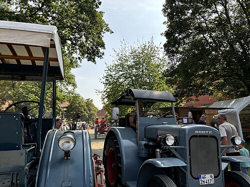 Zwei historische blaugraue Traktoren stehen auf einem großen Hofgelände.